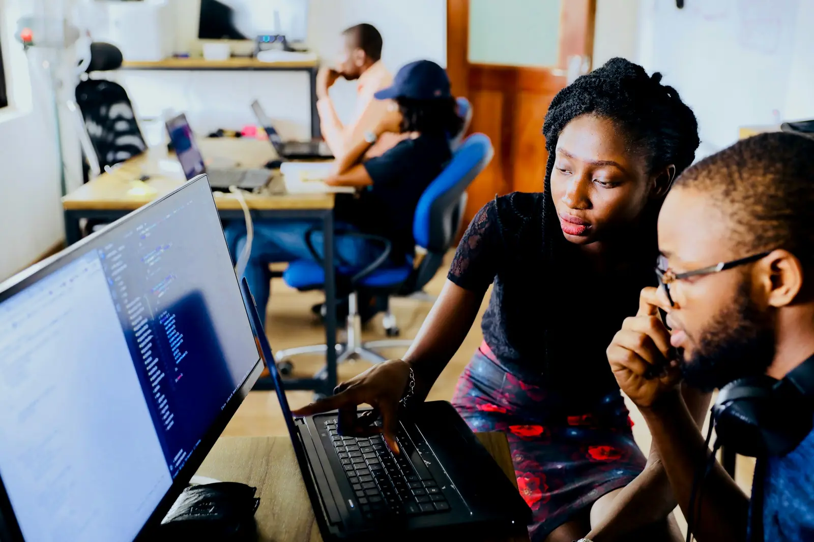 Dois engenheiros africanos analisam código no ecrã de um computador portátil num espaço de trabalho