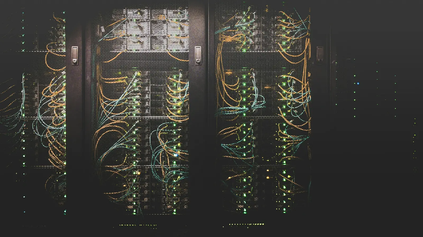 Racks de servidores abertos numa sala escura, com cablagem colorida e indicadores luminosos verdes