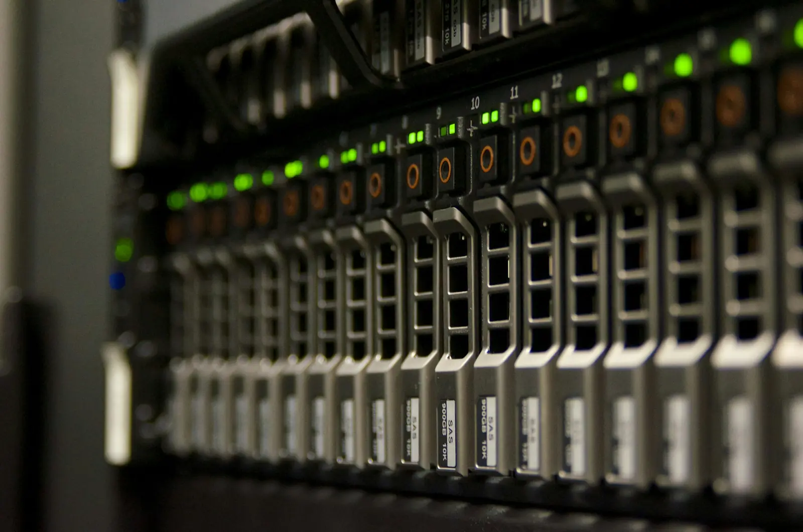 Frente de um servidor em rack com uma fila de gavetas de discos e indicadores luminosos verdes, numa sala escura